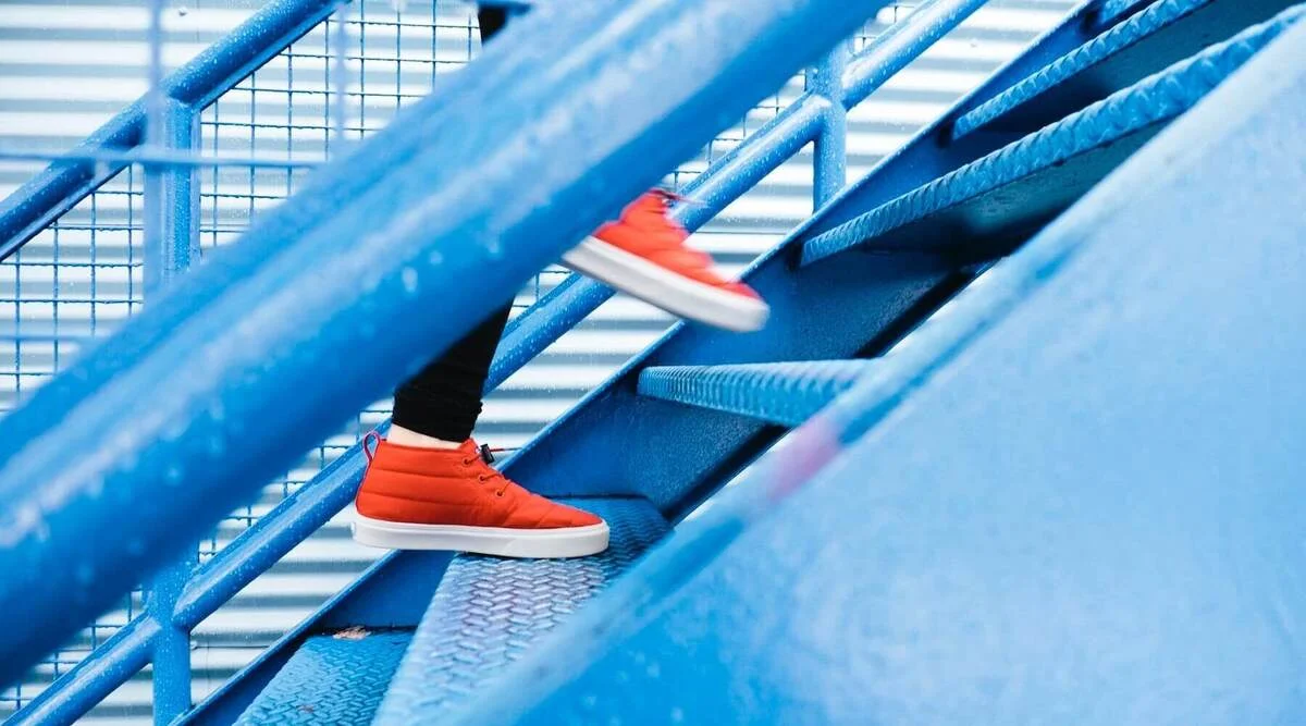 Close-up of a person in orange sneakers climbing a blue metal staircase, one step at a time