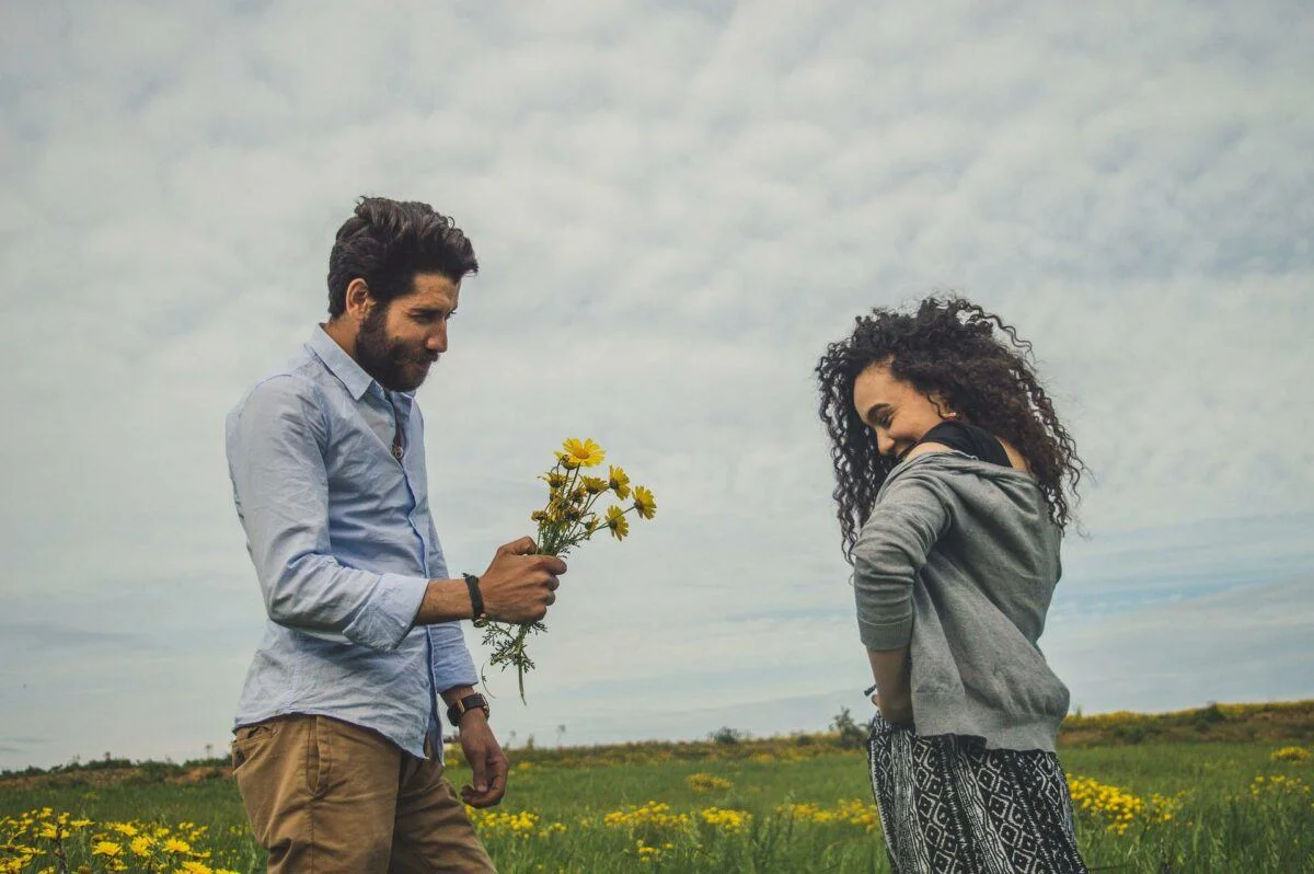 A man offering a handful of yellow wildflowers to a smiling woman in a meadow